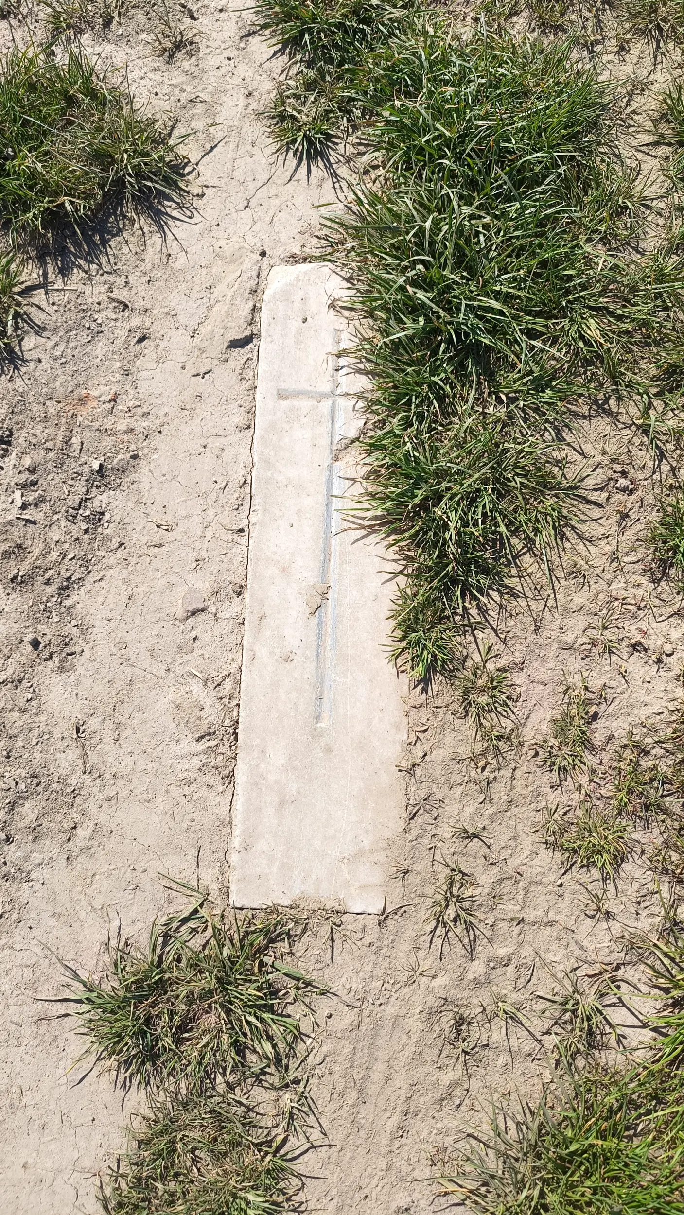 Kawałek kamienia, chyba marmuru, z krzyżem, na środku miedzy
